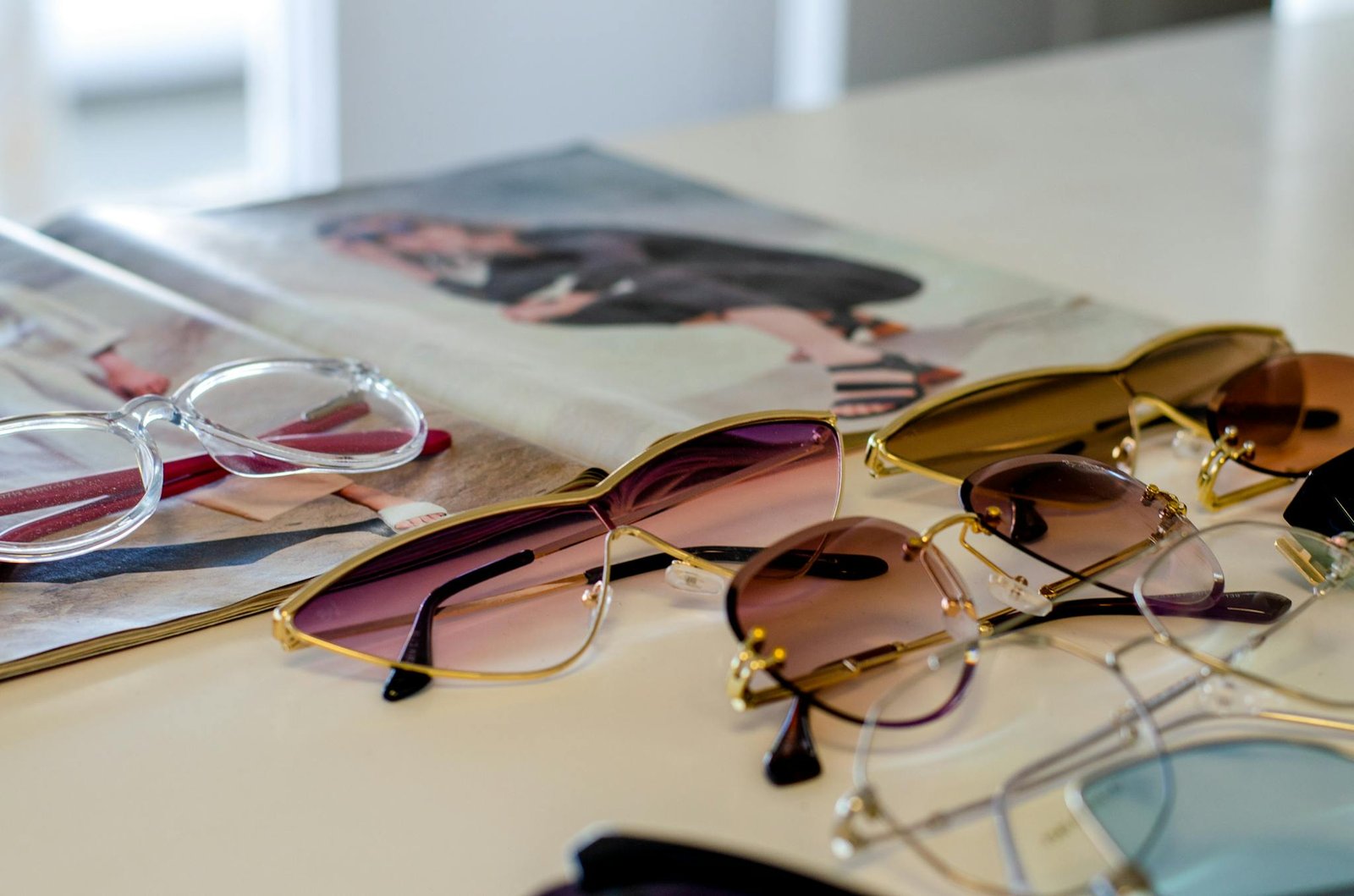 A variety of stylish sunglasses and reading glasses elegantly displayed on a table next to a fashion magazine.